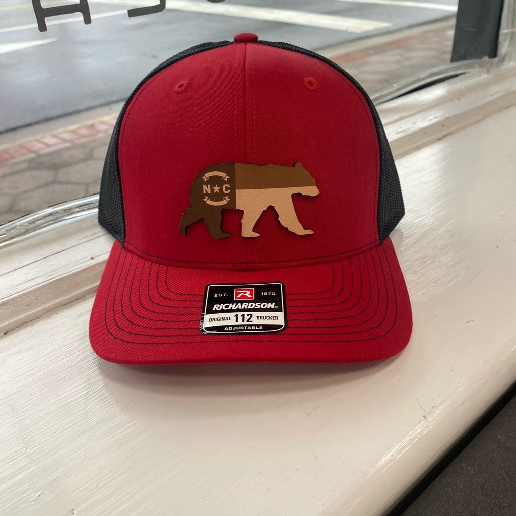 Red and black hat with leather bear emblem that has the North Carolina flag etched into it.  