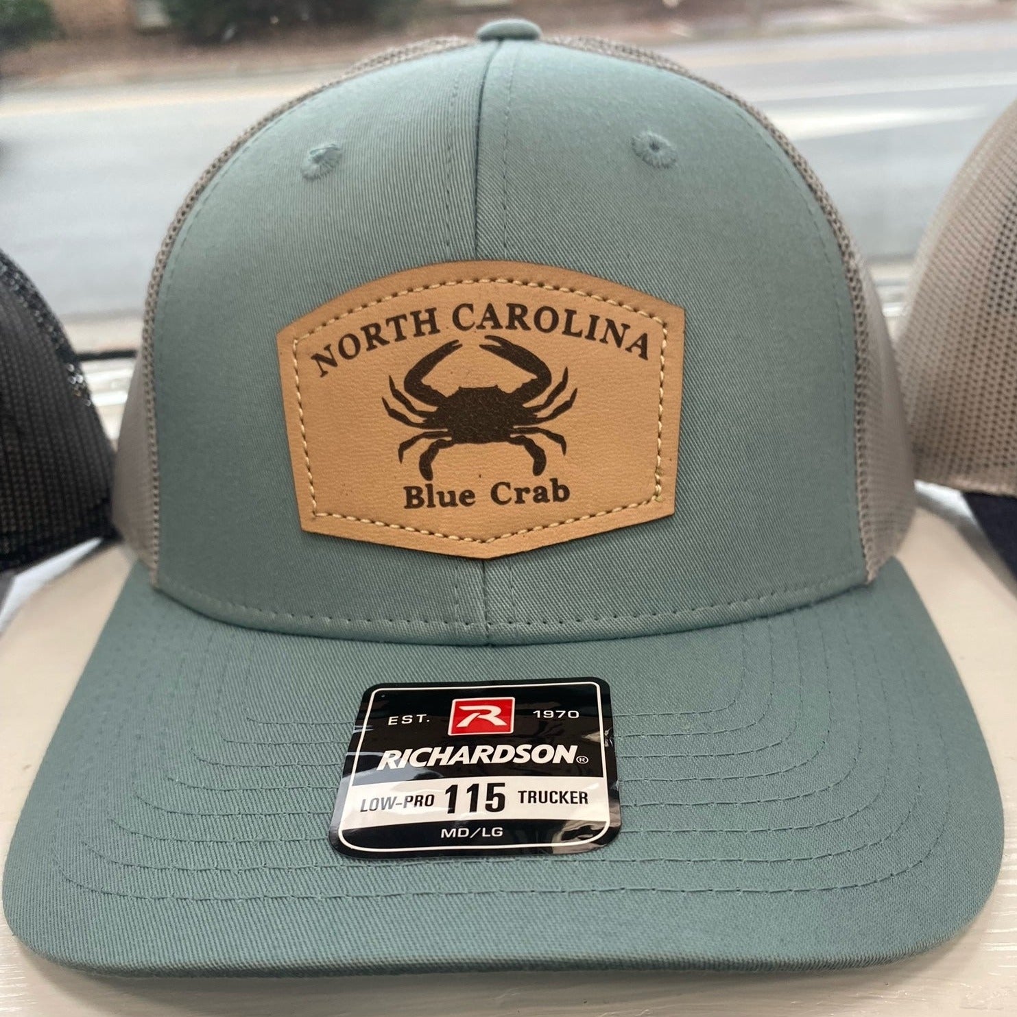 Blue and grey hat with leather emblem that has a blue crab and North Carolina written on it