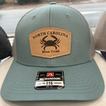Load image into Gallery viewer, Blue and grey hat with leather emblem that has a blue crab and North Carolina written on it
