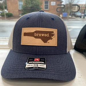 Heathered Navy and grey hat with a leather patch that says "Brewed" inside the shape of North Carolina. 