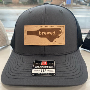 Charcoal grey and black hat with a leather patch that says "Brewed" inside the shape of North Carolina. 