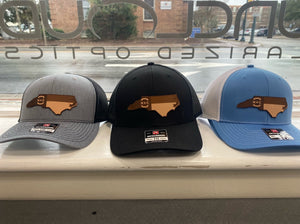Three NC shaped NC flag hats in a window in different colors